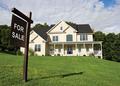 Two-story house for sale with a sturdy foundation, dark roof, large windows, and a porch, set in a lush green yard.
