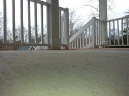 View from a porch looking toward white railings and steps, with bare trees visible in the background.