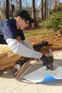 A person skillfully repairs outdoor concrete using a hand-held tool and hose while wearing gloves, sunglasses, and a cap. The application of polyurethane foam ensures durability and precision in sealing the surface.
