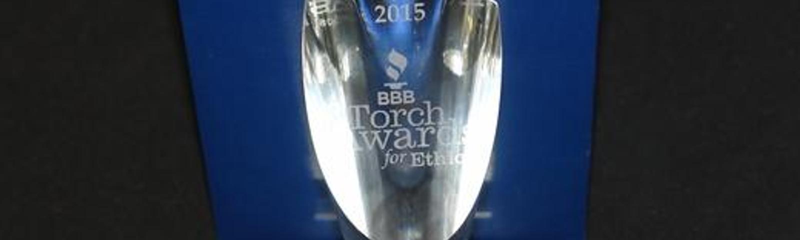 Crystal trophy with "2015 BBB Torch Awards for Ethics" engraved, displayed against a blue background.