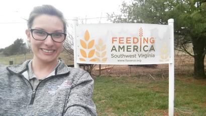 Smiling person in glasses in front of a "Feeding America Southwest Virginia" sign outdoors.