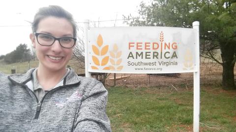 Smiling person in glasses in front of a "Feeding America Southwest Virginia" sign outdoors.