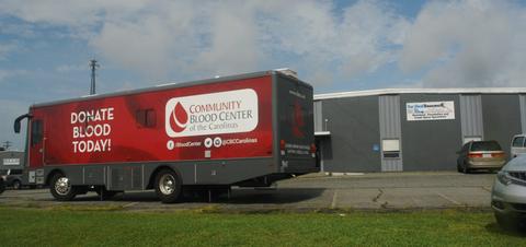 Mobile blood donation truck parked outside a building, with "Donate Blood Today!" written on it.
