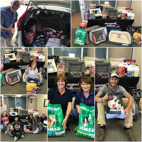 Volunteers pose with pet food and supplies collected for a donation drive, displayed in boxes and bags.