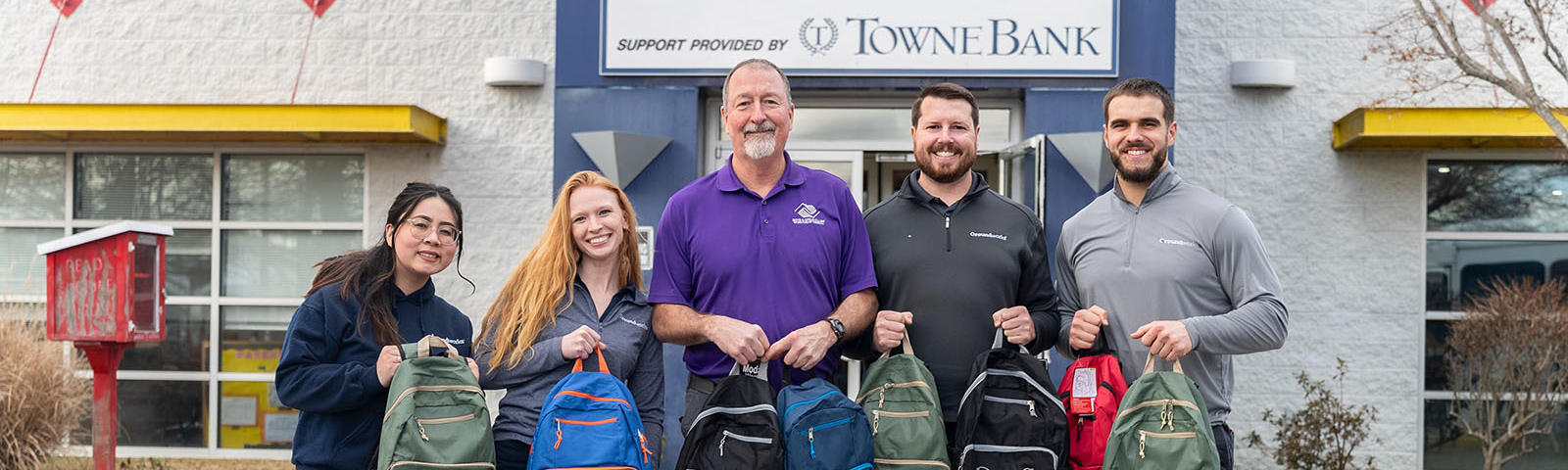 Five people holding backpacks, standing in front of the Boys & Girls Clubs of Southeast Virginia building.
