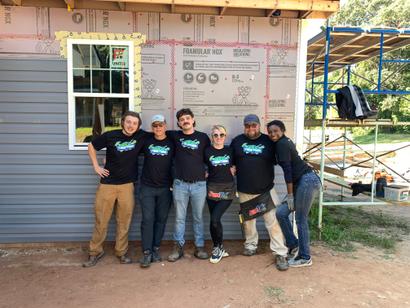 A group of six people in matching shirts posing in front of a house under construction.