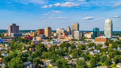 Aerial view of a city skyline with trees in the foreground and buildings rising under a blue sky dotted with clouds, showcasing a landscape shaped by innovative financing.