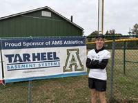 student standing by a Tar Heel Basement Systems banner signifying our company as a sponsor of Apex Middle School Athletics