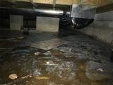 Wet crawl space with exposed ductwork and scattered debris on the ground.