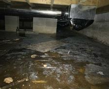 Wet crawl space with exposed ductwork and scattered debris on the ground.