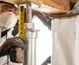 In protective gear, a person measures a support beam with a tape measure, essential for effective crawl space encapsulation.