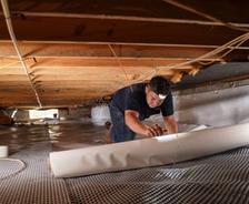 crew member rolling out a vapor barrier in a crawl space
