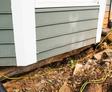 House foundation with visible cracks and erosion, surrounded by dirt and tangled yellow cables.