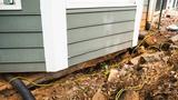 House foundation with visible cracks and erosion, surrounded by dirt and tangled yellow cables.