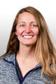 Smiling woman with long hair wearing a blue zip-up jacket, featured in our "meet the team" series against a light, gradient background.