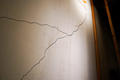 Close-up of a cracked white wall with intersecting black lines and slight shadows.