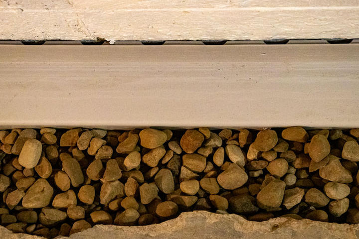 Close-up view of a gutter with light brown rocks beneath it, seamlessly integrated as part of a sump pump installation.
