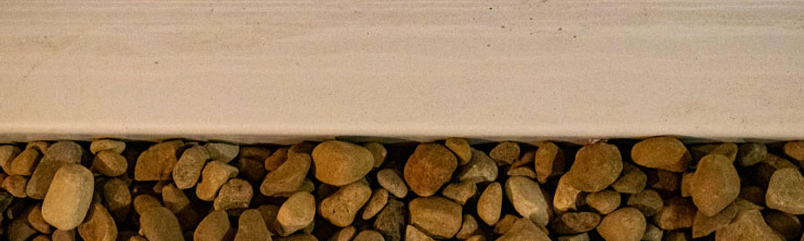 Close-up view of a gutter with light brown rocks beneath it, seamlessly integrated as part of a sump pump installation.