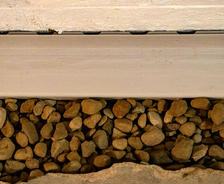 Close-up view of a gutter with light brown rocks beneath it, seamlessly integrated as part of a sump pump installation.