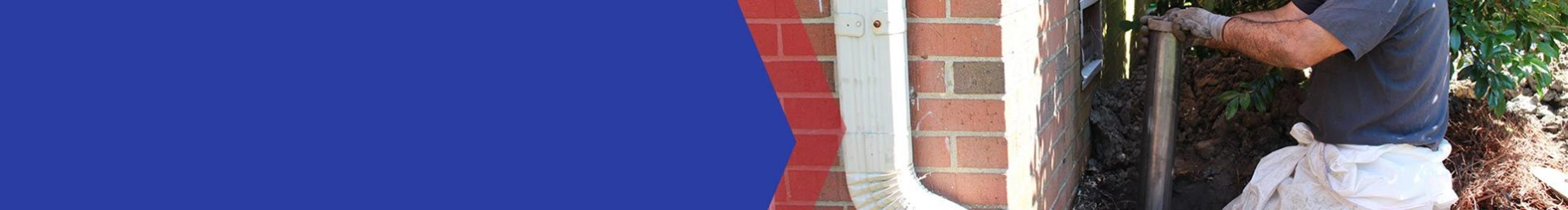 Person gardening beside a brick wall, holding a tool with both hands.