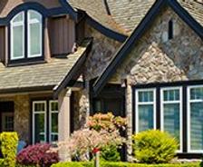 A large, modern house with stone accents, multiple peaked roofs, and a well-maintained garden in front.