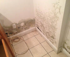 Mold growing on white walls in a tiled corner with a loose cord on the floor.