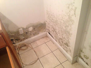 Mold growing on white walls in a tiled corner with a loose cord on the floor.