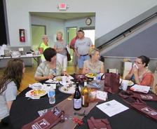People sitting and standing at a dining table in a community hall setting.