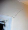 Wall crack extending from a window frame towards the corner of a white wall.