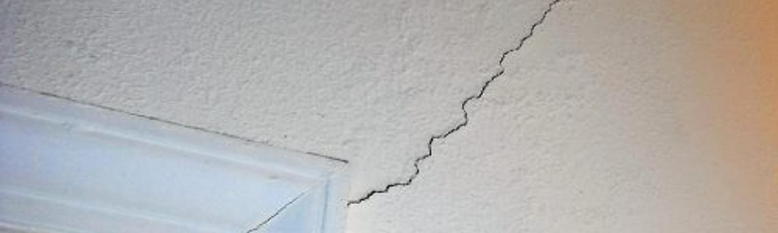 Wall crack extending from a window frame towards the corner of a white wall.