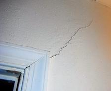 Wall crack extending from a window frame towards the corner of a white wall.
