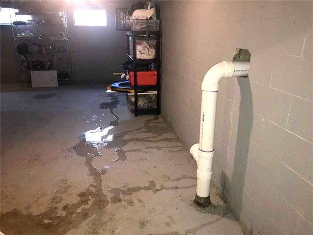 A basement with water leakage, showing puddles on the floor and a white pipe exiting the wall.