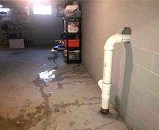 A basement with water leakage, showing puddles on the floor and a white pipe exiting the wall.