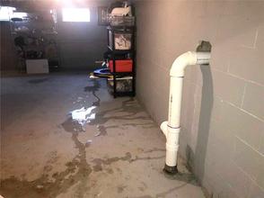 A basement with water leakage, showing puddles on the floor and a white pipe exiting the wall.