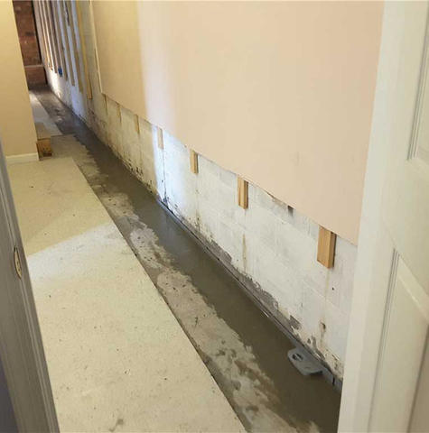 A narrow hallway with freshly poured concrete along the edge of a wall for waterproofing purposes.