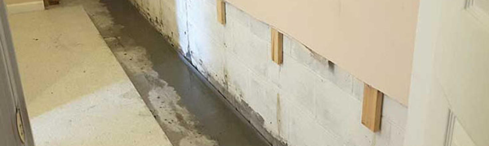 A narrow hallway with freshly poured concrete along the edge of a wall for waterproofing purposes.
