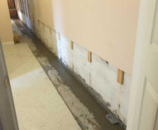 A narrow hallway with freshly poured concrete along the edge of a wall for waterproofing purposes.