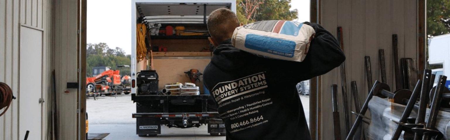 Foundation Recovery Systems crew member carrying sand to box truck.