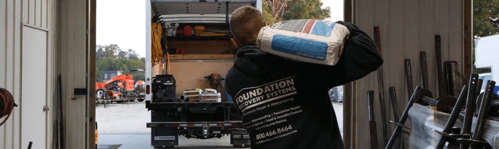 Foundation Recovery Systems crew member carrying sand to box truck.