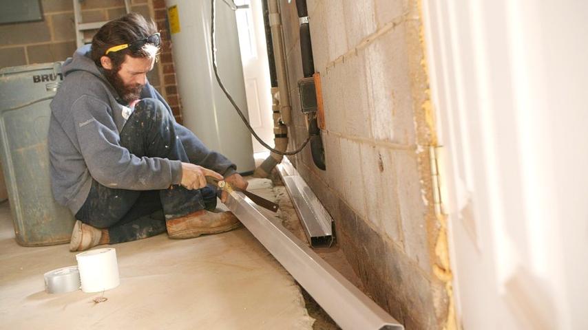 FRS crew member installing interior drainage in basement
