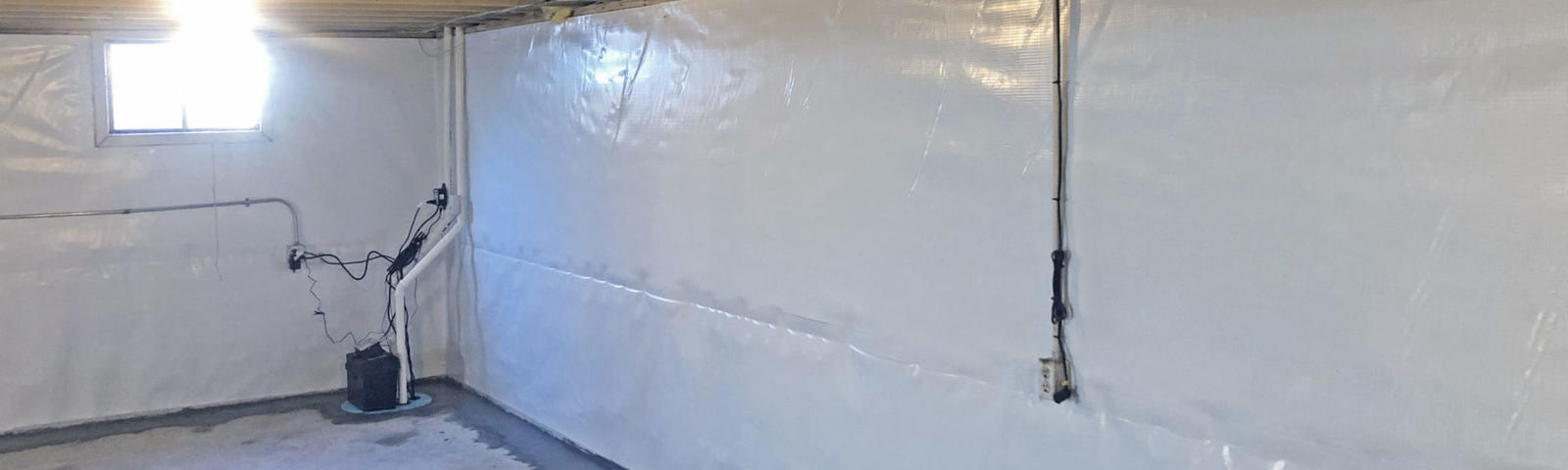 A clean, empty basement features concrete floors and an exposed wooden ceiling. A small window provides natural light, while a discreet vapor barrier ensures moisture control.