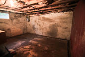 Dimly lit, empty basement with concrete walls and exposed ceiling beams.