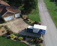 Aerial view of a moving truck parked in the driveway of a suburban house next to a quiet street.
