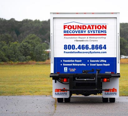 A truck with a "Foundation Recovery Systems" ad parked on a road with trees in the background.