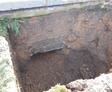 A deep hole in the ground with exposed dirt and a partial view of a brick surface.