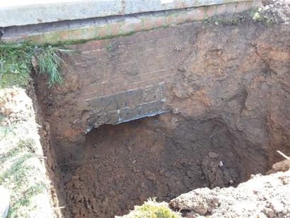 A deep hole in the ground with exposed dirt and a partial view of a brick surface.