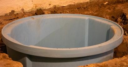 A large blue plastic container, partially embedded in the ground near a concrete wall, hints at hydrostatic pressure problems lurking beneath the surface.