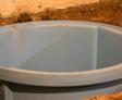 A large, round blue plastic basin, designed to withstand hydrostatic pressure problems, is partially embedded in the ground.