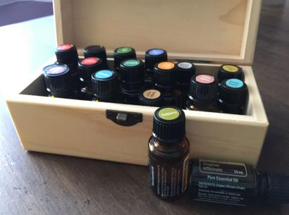 Wooden box with various labeled essential oil bottles on a table to repel basement bugs, one bottle marked "Oregano" in the foreground.