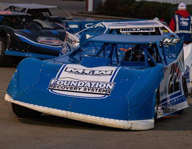 Blue racing car parked with sponsor logos and other race cars in the background.